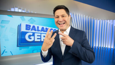 Eleandro Passaia no estúdio do Balanço Geral vestindo terno azul e apontando para três dedos da mão esquerda