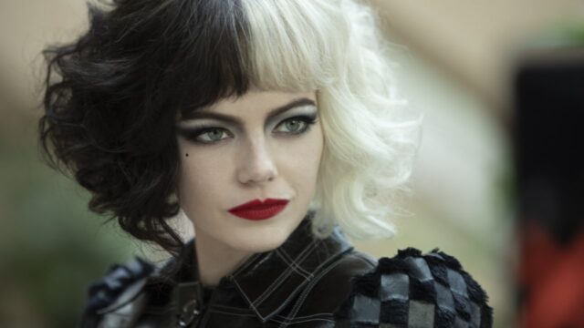 Emma Stone caracterizada como Cruella com cabelo preto e branco, batom vermelho e maquiagem marcante no filme de 2021