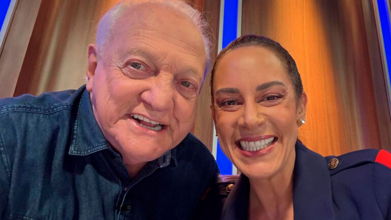 Flávio Ricco e Silvia Abravanel sorrindo lado a lado em ambiente de estúdio iluminado