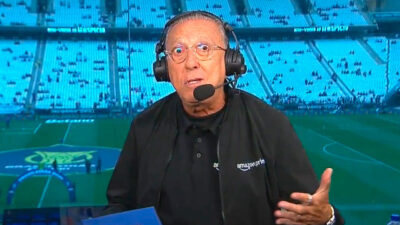 Galvão Bueno com headset no estádio durante transmissão ao vivo do Prime Video com arquibancadas ao fundo