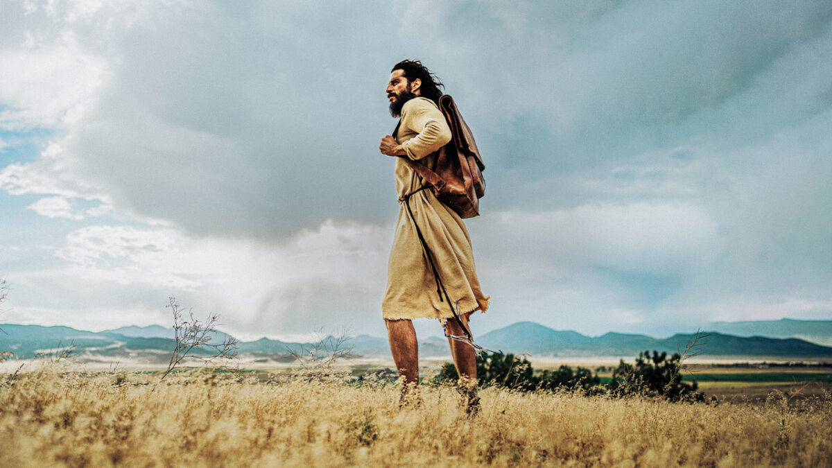 Jonathan Roumie caracterizado como Jesus caminhando em campo aberto na série The Chosen