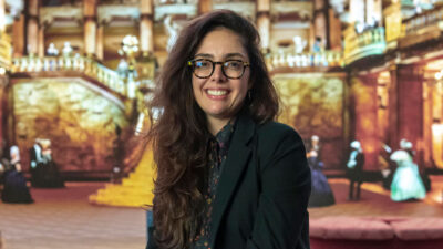 Patricia Pedrosa, diretora do Gênero Humor e Infanto-juvenil da Globo, sorri diante de painel com cenário teatral ao fundo