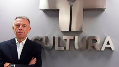 Ricardo Nunes Ribeiro, diretor Comercial da TV Cultura, posa ao lado do logotipo da emissora em parede cinza