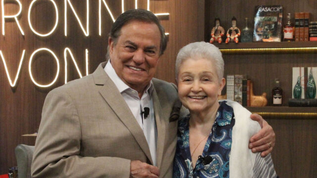 Ronnie Von abraçado a Maria Adelaide Amaral durante participação no programa Companhia Certa, com estante de livros ao fundo