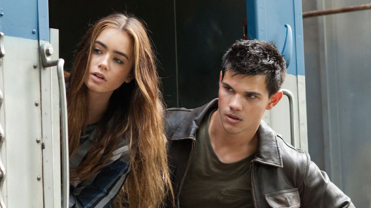 Lily Collins e Taylor Lautner em cena do filme Sem Saída observando o lado de fora de um trem em movimento
