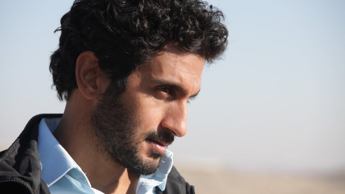 Tsahi Halevi com expressão séria em cena do filme Belém: Zona de Conflito com o céu claro ao fundo