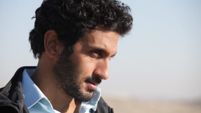 Tsahi Halevi com expressão séria em cena do filme Belém: Zona de Conflito com o céu claro ao fundo