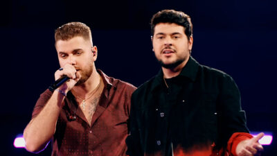 Zé Neto e Cristiano se apresentam no palco durante gravação de show sertanejo com iluminação de fundo azul escuro
