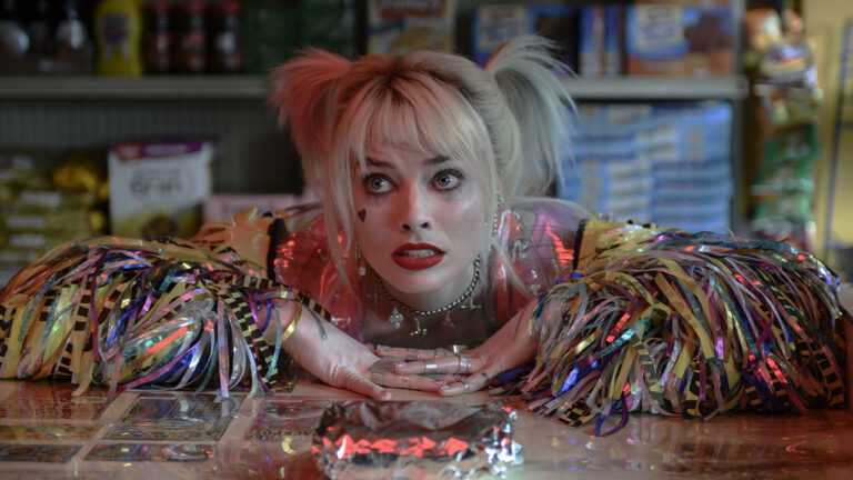 Margot Robbie caracterizada como Arlequina encostada em balcão com expressão surpresa em cena de Aves de Rapina