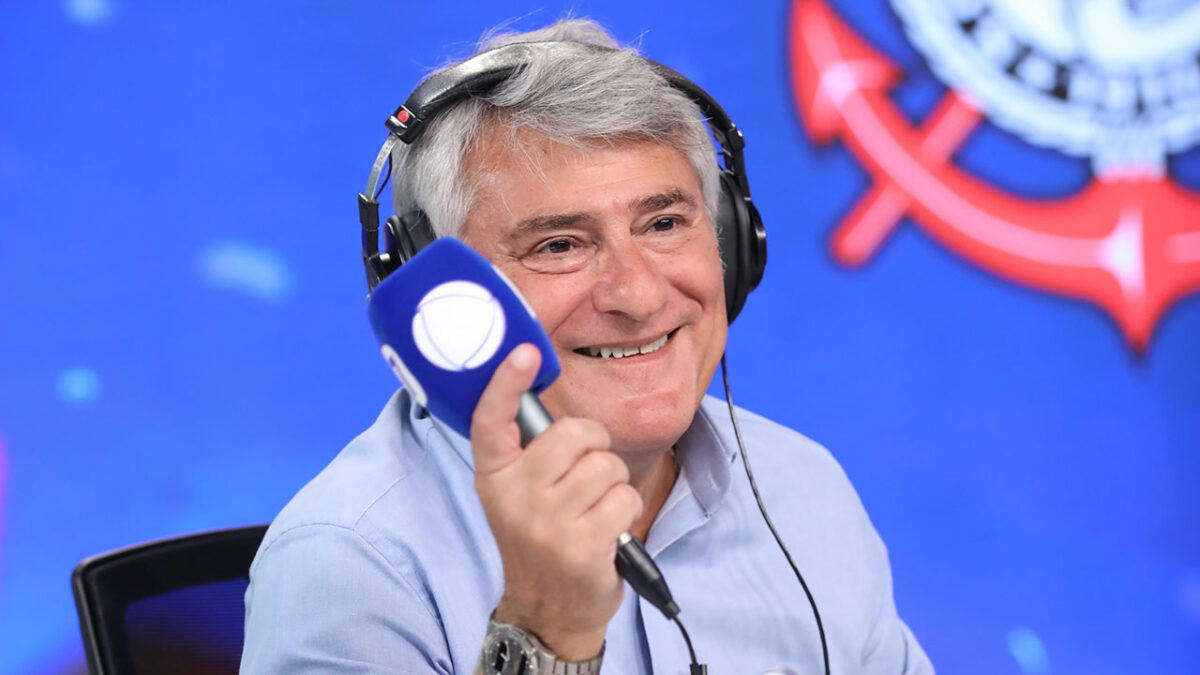 Cléber Machado com fone de ouvido segurando microfone com logo da Record em estúdio com fundo azul