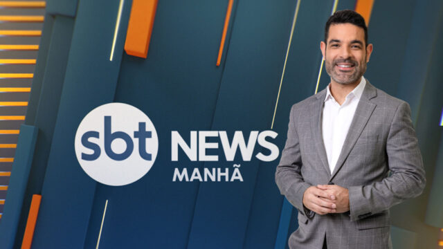 Darlisson Dutra sorrindo em frente ao painel do SBT News Manhã com terno cinza e camisa branca