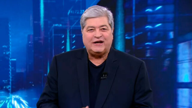 Datena apresenta o programa Tá na Hora do SBT com cenário azul e luzes de cidade ao fundo