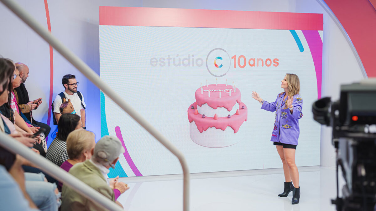 Daiane Fardin em frente a telão com bolo rosa e logo do Estúdio C durante comemoração de 10 anos do programa na RPC