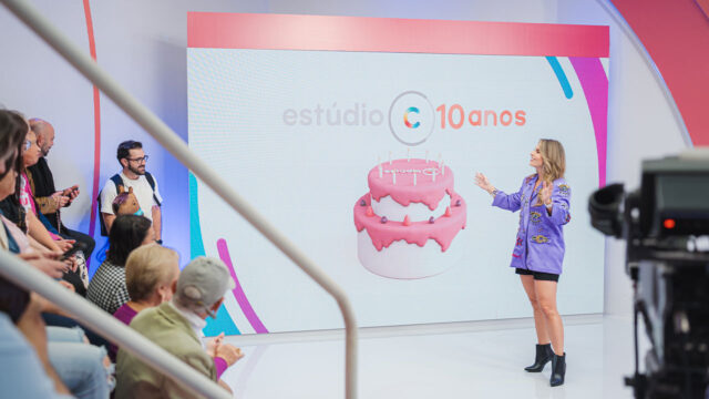 Daiane Fardin em frente a telão com bolo rosa e logo do Estúdio C durante comemoração de 10 anos do programa na RPC