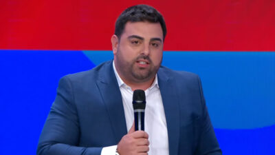 Felipe Macedo, o Macedão, de terno azul e microfone na mão durante apresentação no SBT