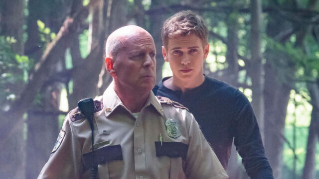 Howell (Bruce Willis) de uniforme policial caminha à frente de Will (Hayden Christensen) em floresta no filme Caçada Brutal