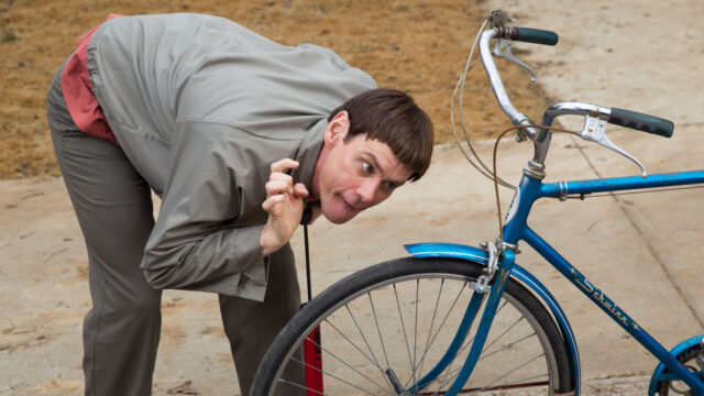 Jim Carrey caracterizado como Lloyd observa pneu de bicicleta em cena de Debi & Lóide 2