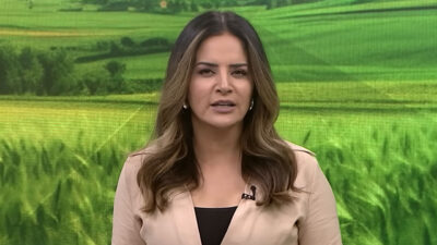 Kelly Godoy apresenta o Record News Rural com imagem de plantação ao fundo no telão do estúdio