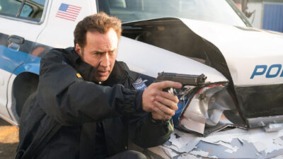 Nicolas Cage como o policial Mike Chandler apontando arma ao lado de viatura danificada em 211: O grande assalto (2018)