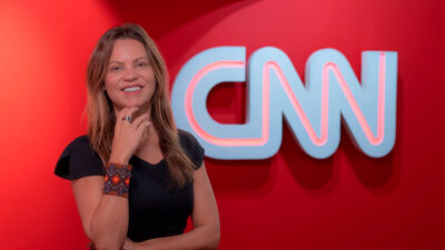 Patricia Ellen sorrindo em frente ao logo da CNN Brasil em parede vermelha