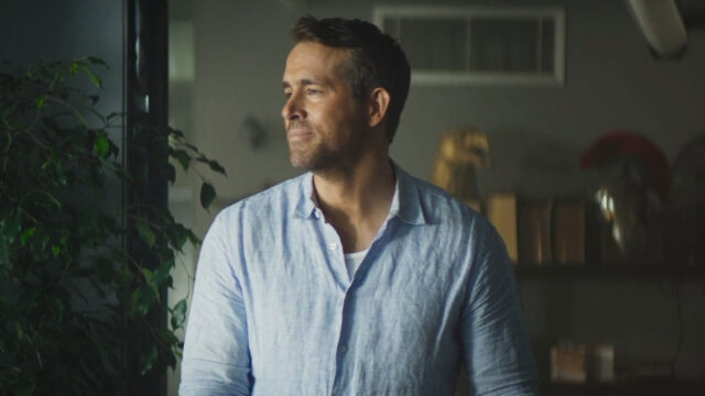 Ryan Reynolds como Michael Bryce usando camisa azul clara e olhando para o lado em cena de Dupla Explosiva 2