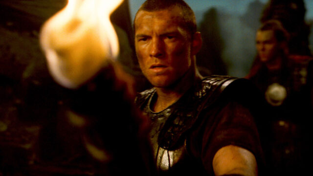 Perseus (Sam Worthington) segurando tocha com expressão determinada em cena de Fúria de Titãs (2010)