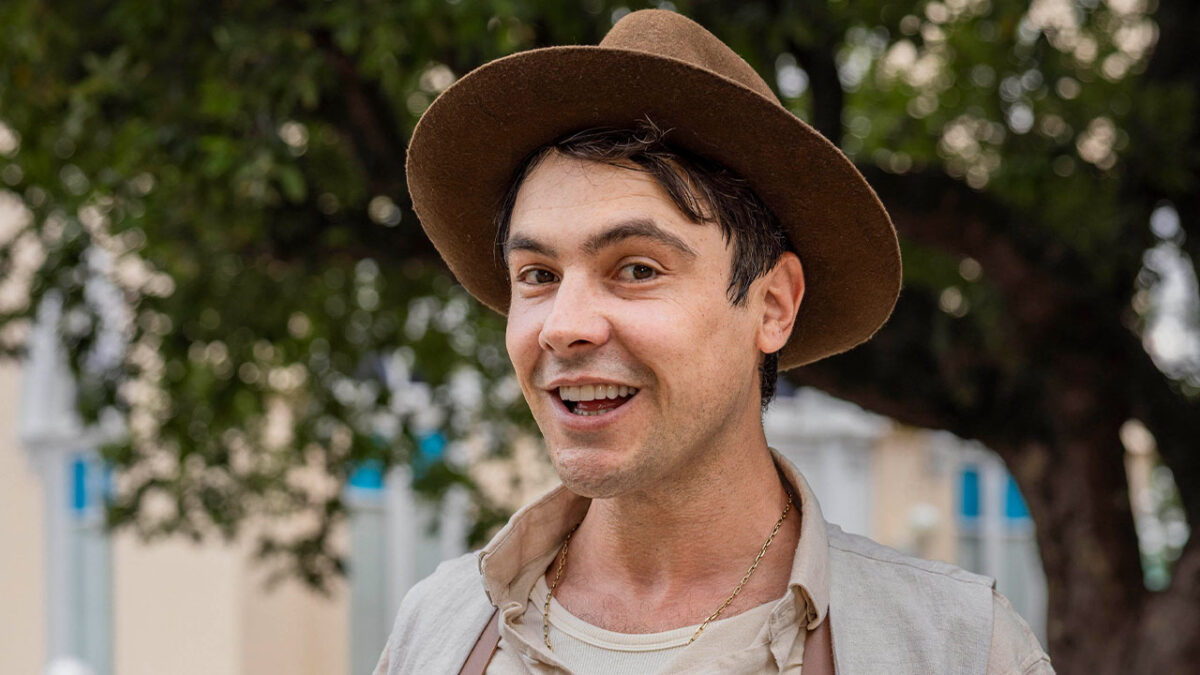 Candinho (Sergio Guizé) sorrindo com chapéu marrom em foto de Êta Mundo Melhor! ao ar livre