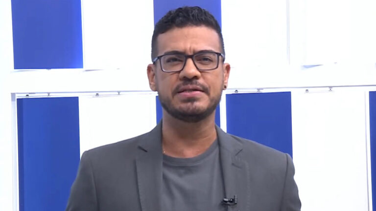 Jhonatã Gabriel em frente a painel azul e branco durante apresentação do TVE Notícias na TVE Bahia