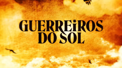 Logo da novela Guerreiros do Sol com letras pretas sobre fundo alaranjado com céu e nuvens ao fundo