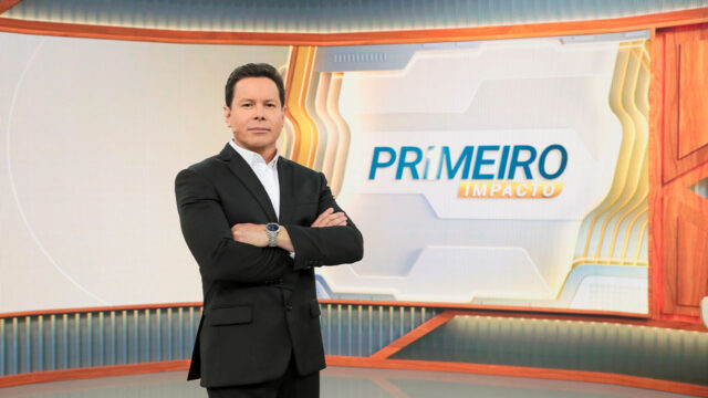 Marcão do Povo de braços cruzados no estúdio do Primeiro Impacto com logotipo do telejornal do SBT ao fundo