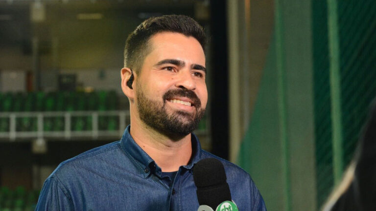 Álvaro Loureiro sorrindo com microfone do SBT em cobertura esportiva dentro de ginásio fechado