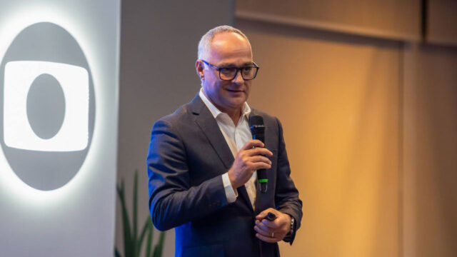 Amauri Soares segurando microfone durante apresentação com logotipo da Globo ao fundo