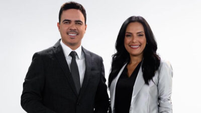 Bruno Pinheiro e Márcia Dantas sorrindo em foto de divulgação da Jovem Pan com fundo branco