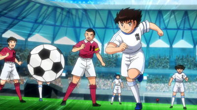 Tsubasa corre com a bola durante partida de futebol em cena do anime Captain Tsubasa dentro de estádio lotado