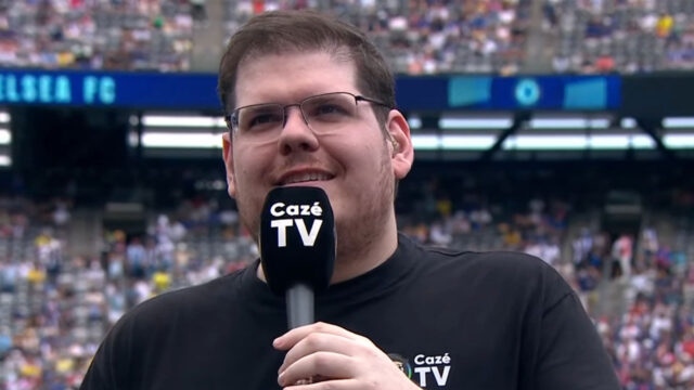 Casimiro Miguel segurando microfone da CazéTV durante transmissão em estádio com público ao fundo