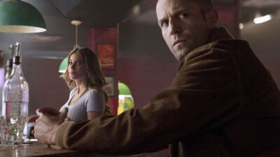 DD (Sofía Vergara) e Nick Wild (Jason Statham) sentados em bar com expressão séria em cena do filme Carta Selvagem (2015)