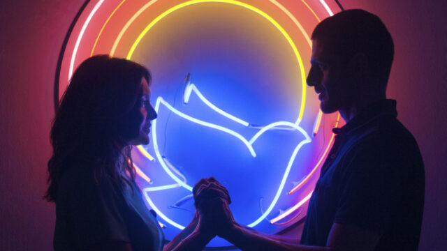Joana (Dira Paes) e Danilo (Julio Machado) se olham e se tocam sob luzes neon coloridas em cena do filme Divino Amor (2019)