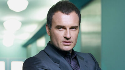 Julian McMahon caracterizado como Christian Troy com expressão séria em corredor da clínica em cena de Nip/Tuck