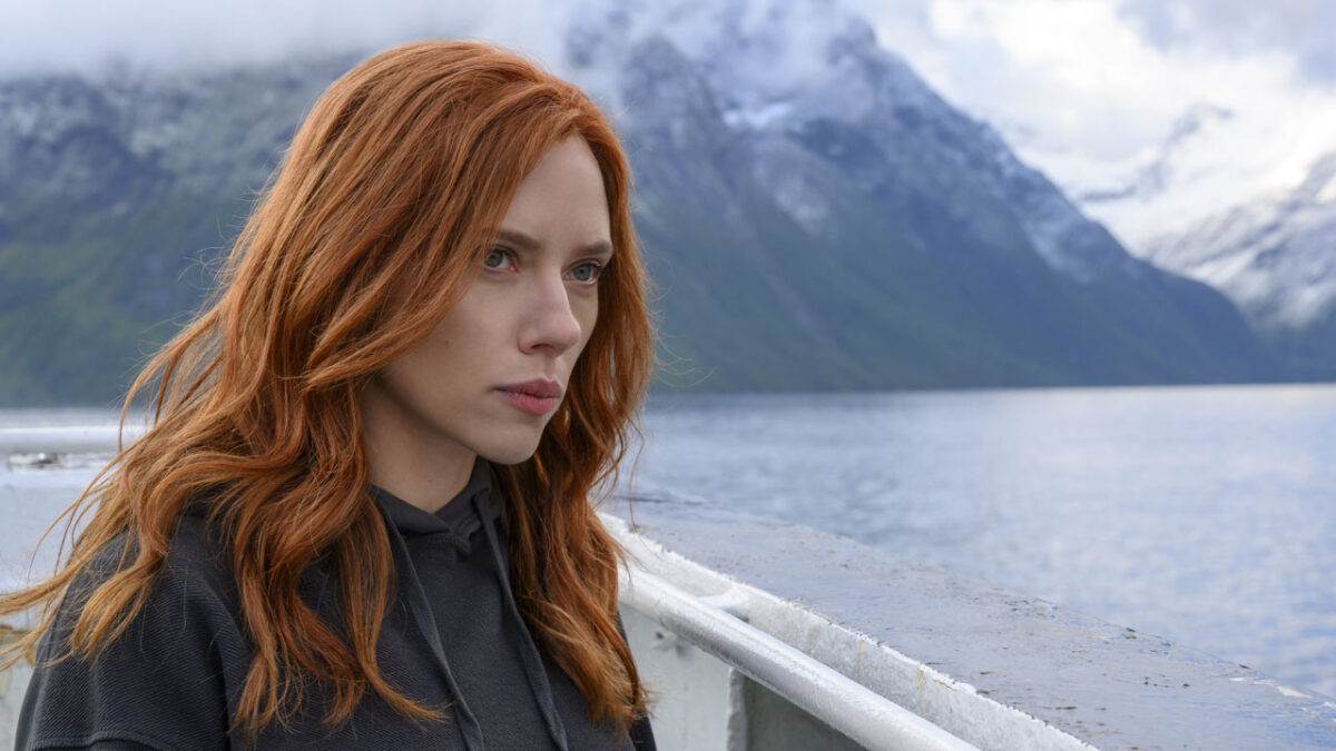 Natasha Romanoff (Scarlett Johansson) séria sobre embarcação com montanhas e lago ao fundo em cena de Viúva Negra