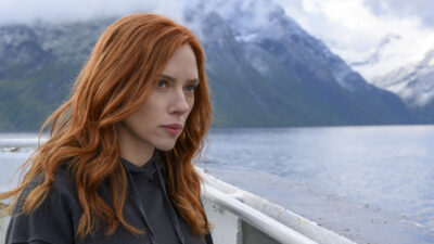 Natasha Romanoff (Scarlett Johansson) séria sobre embarcação com montanhas e lago ao fundo em cena de Viúva Negra