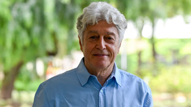 Caco Barcellos, do Profissão Repórter, em área externa, com árvores desfocadas ao fundo.