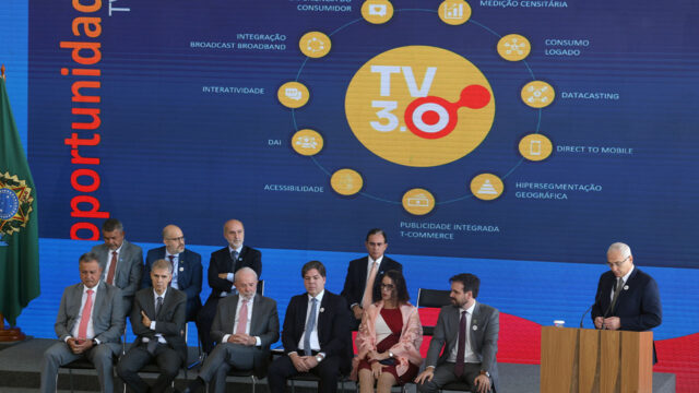 Presidente Luiz Inácio Lula da Silva sentado ao centro em cerimônia no Palácio do Planalto com autoridades diante de painel da TV 3.0