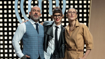 Henrique Fogaça, Helena Rizzo e Paola Carosella posam juntos no estúdio do MasterChef Brasil diante do logo do programa