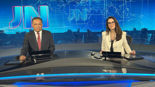 Heraldo Pereira de terno escuro e gravata vermelha e Ana Luiza Guimarães de blazer branco no estúdio do Jornal Nacional