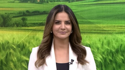 Kelly Godoy apresenta o Record News Rural com cenário de campo verde ao fundo