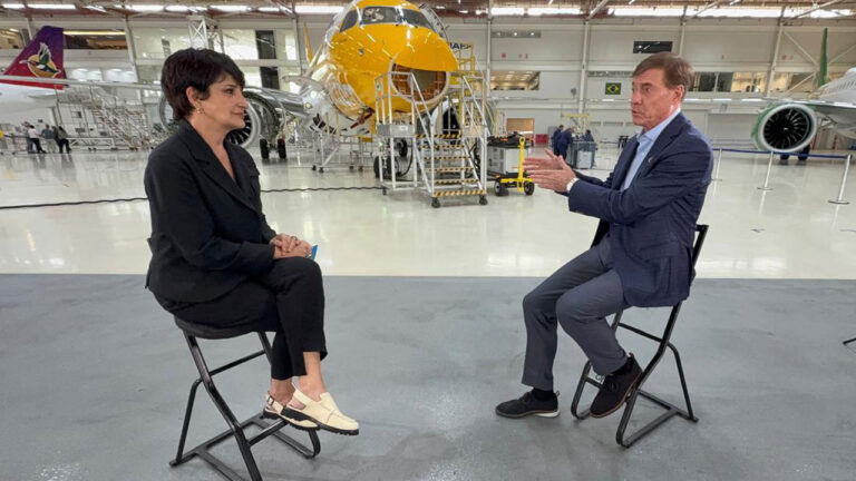 Mônica Waldvogel entrevista Francisco Gomes Neto em hangar da Embraer com aeronaves ao fundo