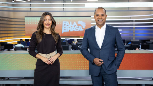 Paloma Poeta e Luiz Fara Monteiro posam no estúdio do Fala Brasil com o logotipo do telejornal ao fundo