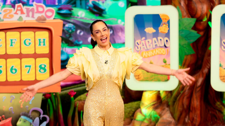 Silvia Abravanel sorridente de braços abertos no novo cenário colorido do programa Sábado Animado do SBT