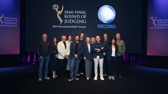 Executivos e profissionais do audiovisual posam juntos no palco em frente a telão com logos do Emmy Internacional 2025 e Record