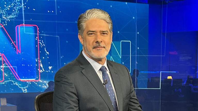 William Bonner de terno azul e gravata estampada apresenta o Jornal Nacional no estúdio da TV Globo com telão azul ao fundo